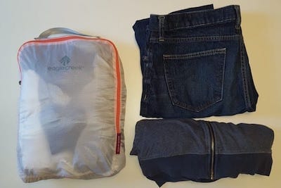 Clothes packed in an organizing bag, jeans and a sweatshirt nearby