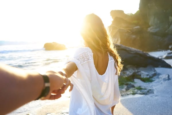 Woman leading man on beach by the hand