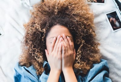 Woman laying on bed, covering her face